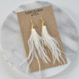 May include: White feather earrings with gold hooks and a brown card with the text "LIBBY & SMEE handmade in WESTFIELD, NJ"