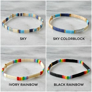 May include: Four different styles of beaded bracelets. The bracelets are made with small, square beads in various colors, including blue, white, ivory, black, red, orange, yellow, green, and purple. The bracelets are arranged in a grid pattern, with each bracelet labeled with its name: "SKY", "SKY COLORBLOCK", "IVORY RAINBOW", and "BLACK RAINBOW".