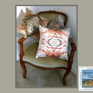 May include: A wooden armchair with a beige fabric seat and three patterned throw pillows. The pillows feature abstract designs in shades of brown, beige, and orange. The chair is in a room with a light-colored wall.