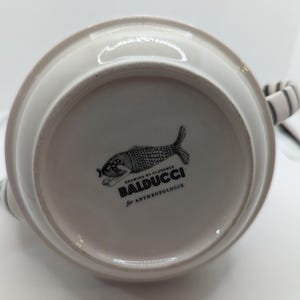 May include: White ceramic pitcher with a black and white fish design. The bottom of the pitcher has the text "Drawing by Florence Baldducci for Anthropologie".
