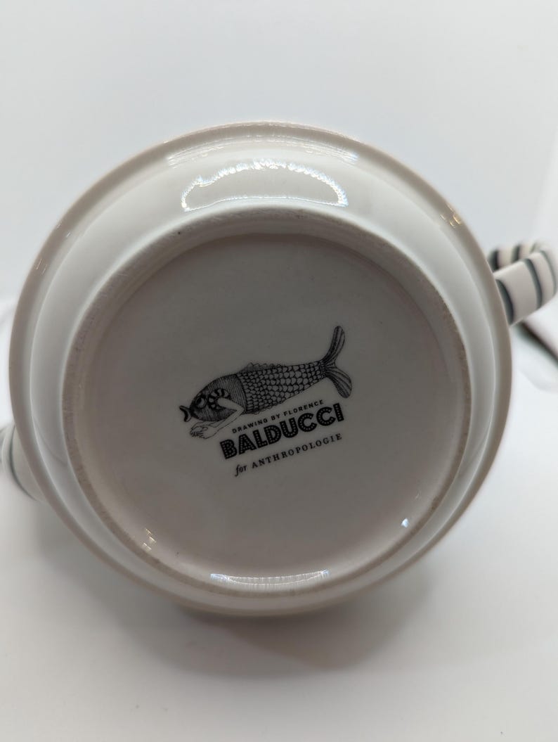 May include: White ceramic pitcher with a black and white fish design. The bottom of the pitcher has the text "Drawing by Florence Baldducci for Anthropologie".