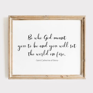 May include: A framed print with a white background and black text that reads "Be who God meant you to be and you will set the world on fire." The text is attributed to Saint Catherine of Siena.