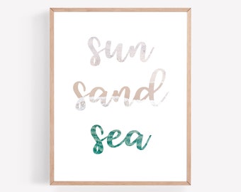 May include: A framed print with the text "Sun Sand Sea" in a white background. The words are stylized with a beach-themed design. The word "Sun" is in a light pink color, "Sand" is in a light brown color, and "Sea" is in a teal color.