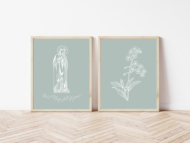 May include: Two framed prints with a light blue background. The print on the left features a line drawing of the Virgin Mary with the text "Hail Mary full of grace". The print on the right features a line drawing of a forget-me-not flower.