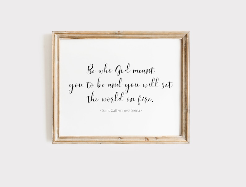 May include: A framed print with a white background and black text that reads "Be who God meant you to be and you will set the world on fire." The text is attributed to Saint Catherine of Siena.