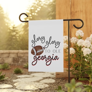 May include: White garden flag with a brown and white football and the text "glory glory to ole georgia" in black with a red outline.