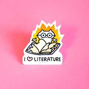 May include: A white cat wearing glasses is sitting inside an open book with flames coming out of the book. The text "I &hearts; LITERATURE" is below the book.