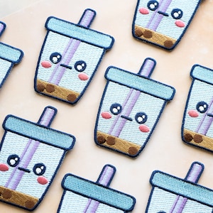 May include: Eight embroidered patches of a cartoon boba tea cup with a straw, brown boba pearls, and a cute face. The patches are on a light brown background.