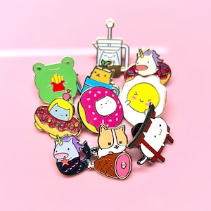 Puede incluir: Una colección de pines de esmalte coloridos con animales de dibujos animados, comida y otros diseños caprichosos. Los pines son todos de color dorado y tienen un acabado brillante.
