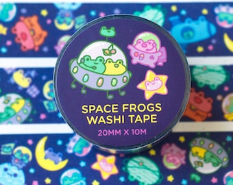 May include: A roll of washi tape with a dark blue background and a repeating pattern of frogs in spaceships, stars, and moons. The tape is labeled "Space Frogs Washi Tape 20mm x 10m".