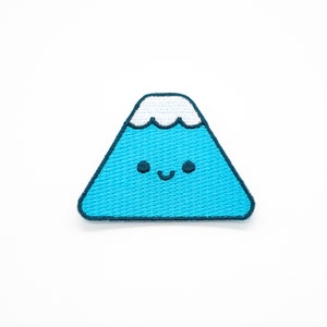 May include: A blue and white embroidered patch of a smiling mountain with a white snowcap.