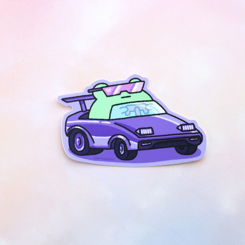 Peut inclure: Un autocollant repr&eacute;sentant une grenouille verte portant des lunettes de soleil et conduisant une voiture violette. La voiture a un aileron et des phares. La grenouille regarde droit devant.