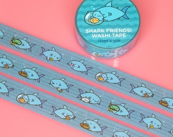 May include: Three rolls of blue washi tape with a repeating pattern of cartoon sharks. The tape is labeled "Shark Friends! Washi Tape 15mm x 10m".