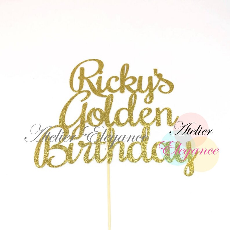May include: A gold glitter cake topper with the words "Ricky's Golden Birthday" in a cursive font. The topper is attached to a wooden stick for easy insertion into a cake. The background is white.