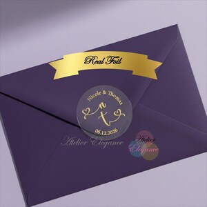 May include: A deep purple envelope with a gold foil banner reading "Real Foil." A clear, circular sticker displays the names "Nicole & Thomas" with a stylized "n" and "t" and the date "06.12.2026" in gold, decorated with hearts.