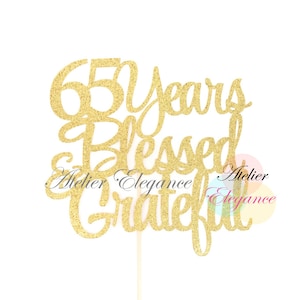May include: Gold glitter cake topper with the text "65 Years Blessed & Grateful".
