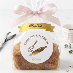 May include: A clear plastic bag containing a small loaf of bread, tied with a light pink ribbon. A white circular sticker features the gold foil text "FROM THE KITCHEN OF" and "KAYLEE" with a gold foil whisk and rolling pin graphic.