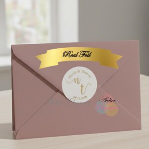 May include: A dusky pink envelope with a gold foil banner reading "Real Foil." A white circular sticker displays the names "Nicole & Thomas" and the date "06.12.2016."