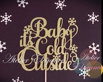 May include: Gold glitter cake topper with the text "Baby it's Cold Outside" and snowflakes.
