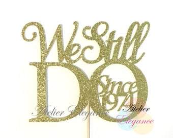 May include: Gold glitter cake topper with the words "We Still Do" and "Since 1974".