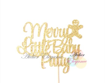 May include: Gold glitter cake topper with the text "Merry Little Baby" and a small gingerbread person. The topper is on a wooden stick.