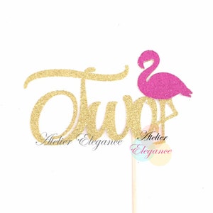 May include: Gold glitter "Two" cake topper with a pink glitter flamingo. The topper is on a wooden stick and is perfect for a tropical themed birthday party.