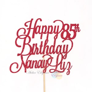 May include: Red glitter cake topper with the text "Happy 85th Birthday Nana Liz" and the words "Atelier Elegance" at the bottom.
