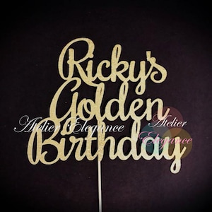 May include: A gold glitter cake topper with the words "Ricky's Golden Birthday" in a cursive font. The topper is on a thin, silver stick for insertion into a cake. The background is a dark, solid color.