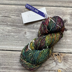 Peut inclure: Une pelote de laine dans un motif multicolore de vert, marron, rouge et jaune. La laine est étiquetée "886 DIANA" et "ECCHA" sur une étiquette blanche.