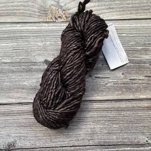 May include: A skein of dark brown yarn with a subtle marled effect. The yarn is made of wool and is suitable for knitting or crocheting.