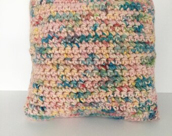 Könnte beinhalten: Ein farbenfrohes gehäkeltes Kissen mit einem Farbschema in Rosa, Gelb, Blau und Grün. Das Kissen ist aus einem dicken Garn gefertigt und hat eine weiche, strukturierte Oberfläche.