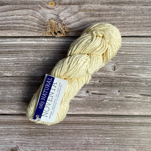 May include: A skein of off-white yarn with a blue and white label that reads "063 NATURAL NOVENTA" and includes information about the yarn's composition and care instructions.