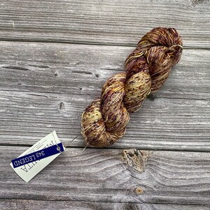 May include: A skein of yarn in shades of brown, cream, and gold with a speckled pattern. The yarn is wrapped around itself and has a tag attached that reads "ITALIA 343 LEGEND".
