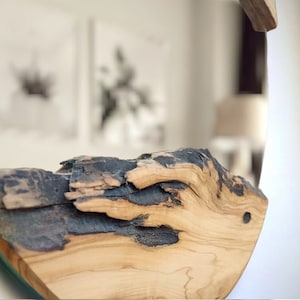 Puede incluir: Un espejo de pared circular con un marco de madera natural gruesa con borde vivo. La madera muestra una veta de color tostado claro con secciones oscuras, carbonizadas o negras desgastadas a lo largo de la superficie irregular.