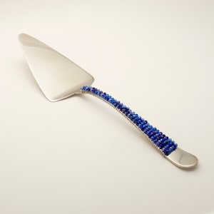 May include: A silver cake server with a blue and purple beaded handle.