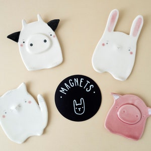 Peut inclure: Ensemble de cinq aimants en céramique représentant des animaux. Les aimants sont blancs avec des accents roses et noirs. Les motifs comprennent une vache, un lapin, un chat, un cochon et un lapin. Les aimants sont étiquetés "MAGNETS."