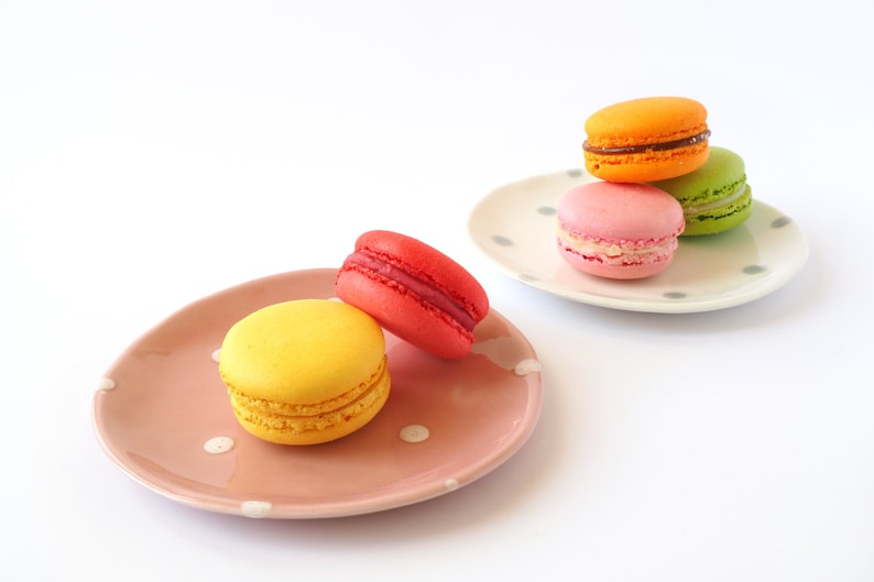May include: A plate with four colourful macarons, two on a pink plate and two on a white plate with grey polka dots.