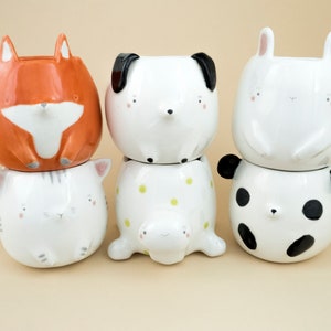 May include: Four ceramic planters shaped like animals. A fox, a dog, a cat, and a panda. The planters are stacked on top of each other.