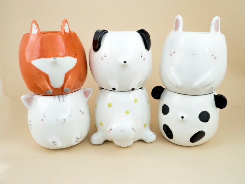 May include: Four ceramic planters shaped like animals. A fox, a dog, a cat, and a panda. The planters are stacked on top of each other.