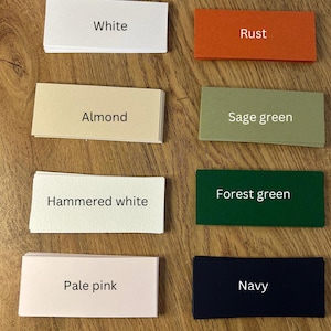 Peut inclure: Un ensemble d'échantillons de couleurs sur une surface en bois. Les échantillons présentent les couleurs suivantes : blanc, rouille, amande, vert sauge, blanc martelé, vert forêt, rose pâle et marine. Chaque échantillon porte le nom de la couleur.
