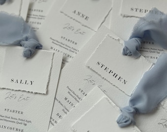 May include: A set of white cards with a torn edge, each with a name and the text "Let's Eat" written in cursive. The cards are arranged in a stack, with the top card showing the name "Sally".
