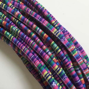 May include: A close-up of a bundle of colorful striped fabric cord. The cord is made of woven cotton and has a variety of colors, including pink, purple, green, yellow, and blue.