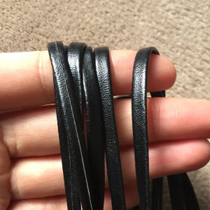 Può includere: Primo piano di un cordoncino in pelle nera, che mostra la trama e lo spessore del materiale.