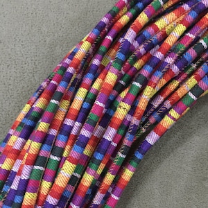 May include: A close-up of a bundle of colorful striped fabric cord. The cord is made of woven fabric and has a variety of colors, including red, orange, yellow, green, blue, purple, and pink.