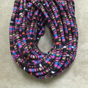 May include: A close-up of a multi-colored woven cord with black, pink, blue, green, and orange stripes. The cord is coiled in a circle.