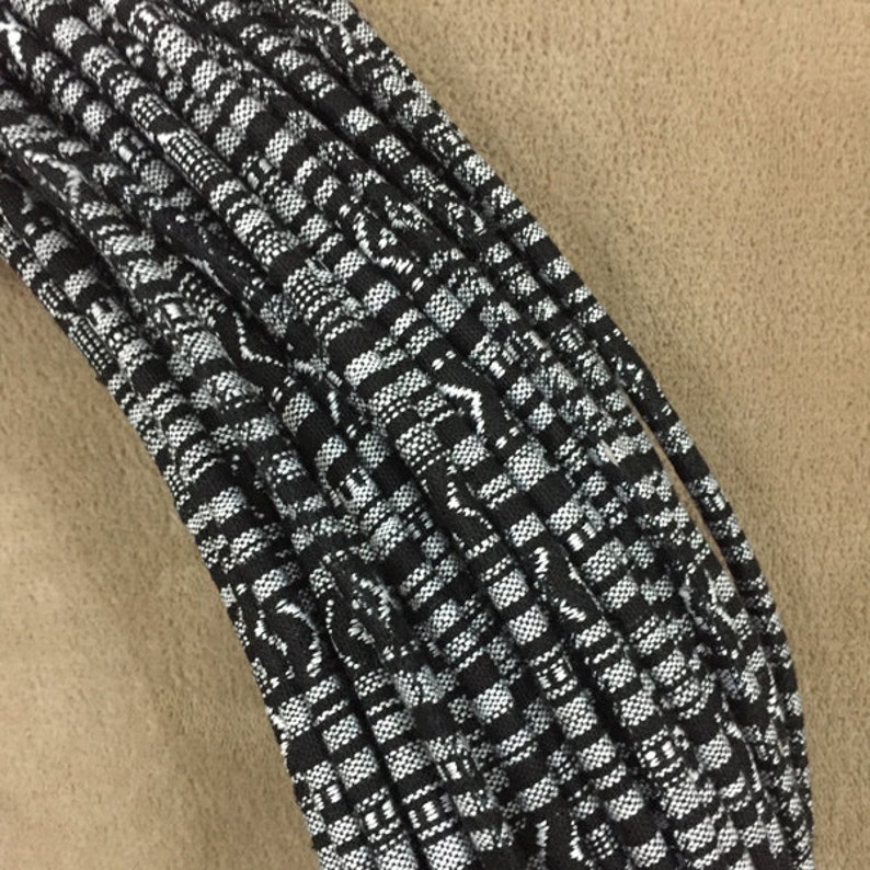 May include: A close-up of a bundle of black and white patterned shoelaces. The shoelaces are made of a woven fabric and have a geometric design.