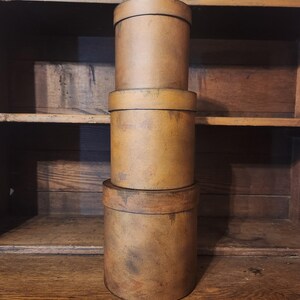 May include: Three stacked round wooden boxes with a distressed brown finish. The boxes are stacked on a wooden shelf.