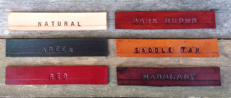 Pu&ograve; includere: Sei campioni di pelle in diversi colori e finiture. I campioni sono etichettati "Naturale", "Marrone scuro", "Verde", "Sella Tan", "Rosso" e "Marrone".