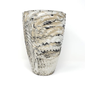 May include: A tall, textured vase with a unique, swirling pattern in shades of white, beige, and black. The vase has a wide top and tapers down to a narrower base. The design gives the vase a marbled appearance.