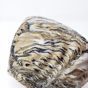 May include: A white, black, and gold marbled planter with a wavy pattern. The planter has a textured surface and is made of concrete.